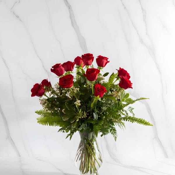 Red roses arranged in a clear glass vase with greenery