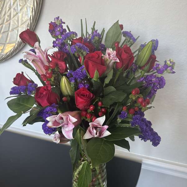 Bouquet of red roses, pink lilies, and purple flowers in a clear glass vase
