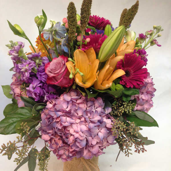 Mixed bouquet with pink hydrangeas, orange lilies, and magenta daisies in burlap wrap