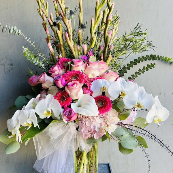 Tall bouquet of pink roses, white orchids, and gerbera daisies in a glass vase