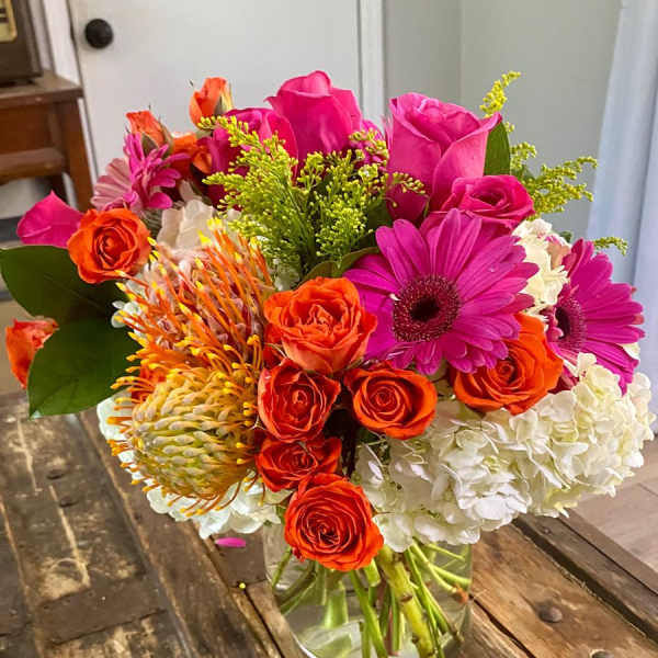 Bright mixed bouquet in a clear glass vase with pink, orange, and white flowers.