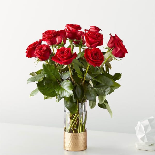 Red roses arranged in a clear glass vase with a gold base