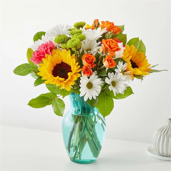 Bouquet of sunflowers, daisies, and orange roses in a blue glass vase
