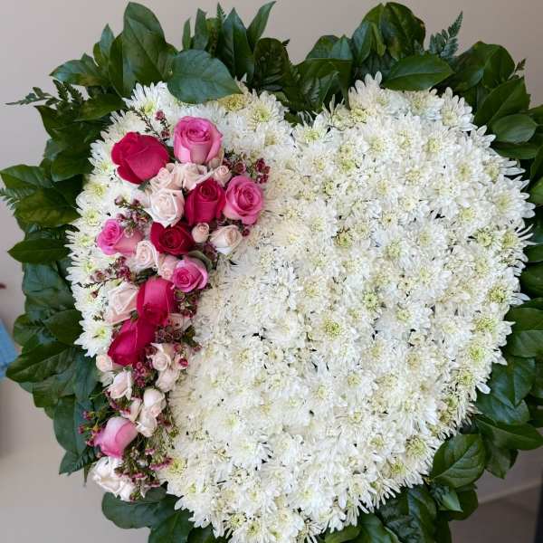Heart-shaped white chrysanthemum wreath with pink roses and a green leaf border