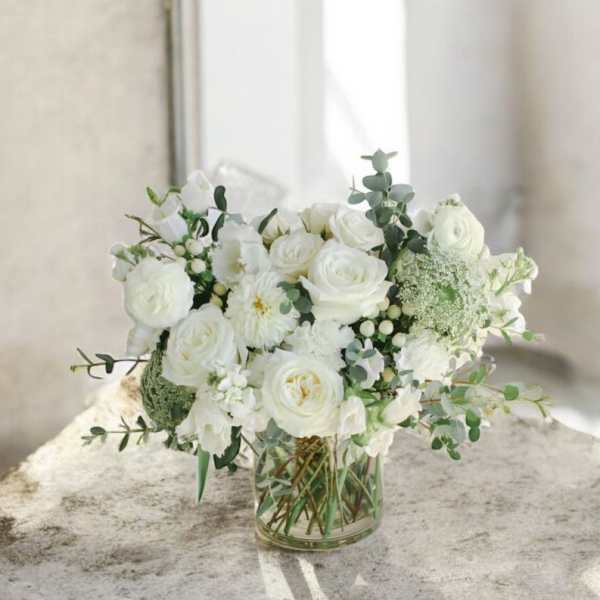 White roses and mixed white blooms arranged in a clear glass vase