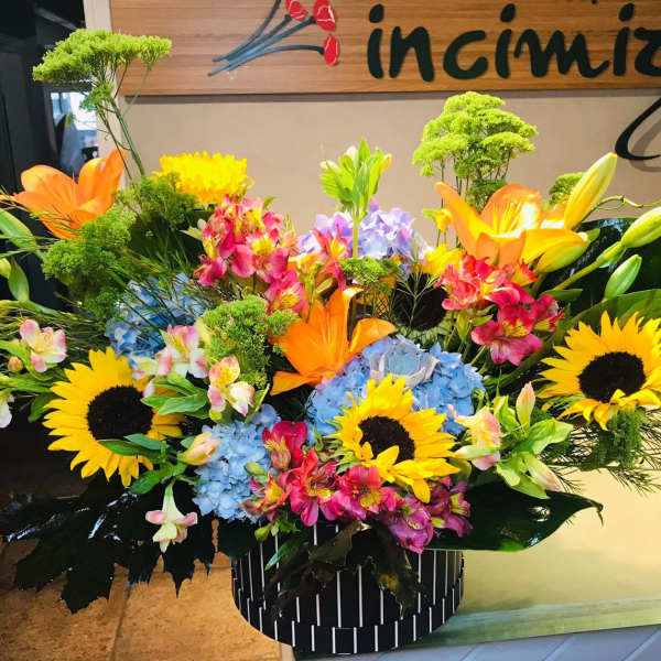 Large mixed flower arrangement with sunflowers, lilies, hydrangeas, and orchids in a striped container