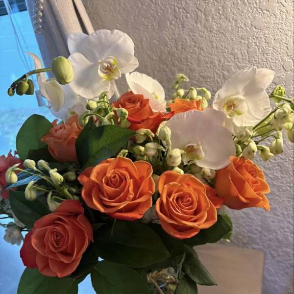 Orange roses and white orchids in a clear glass vase