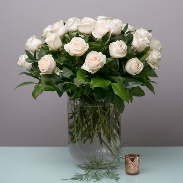 White roses arranged in a clear glass vase with greenery.