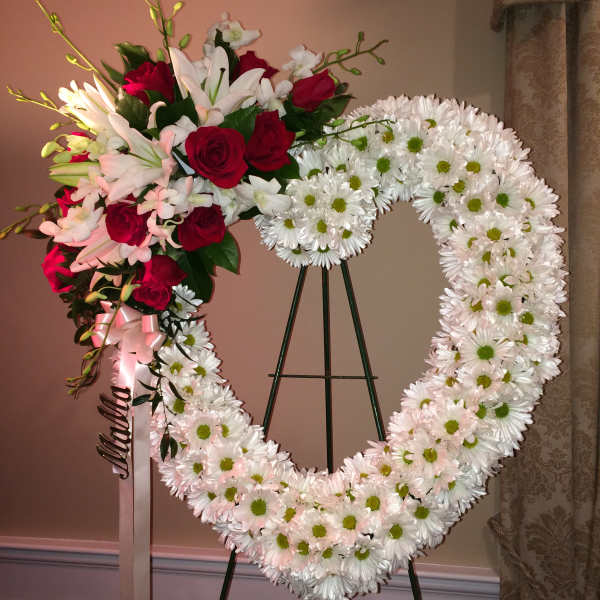 Heart-shaped floral wreath with red roses and white daisies on a stand
