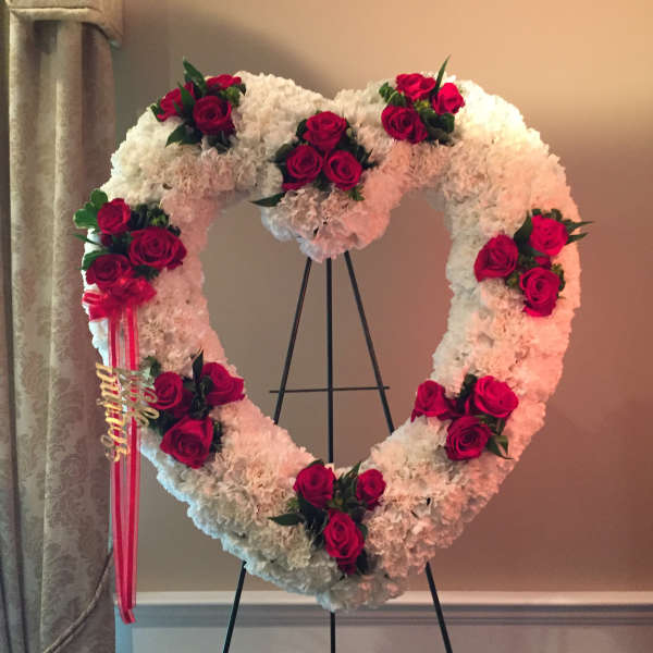 Heart-shaped floral wreath with red roses and white blooms on an easel