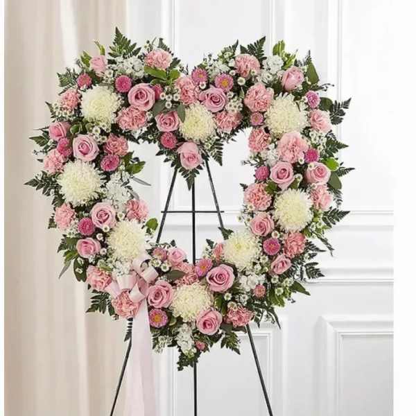 Heart-shaped floral wreath with pink roses and white blooms on an easel