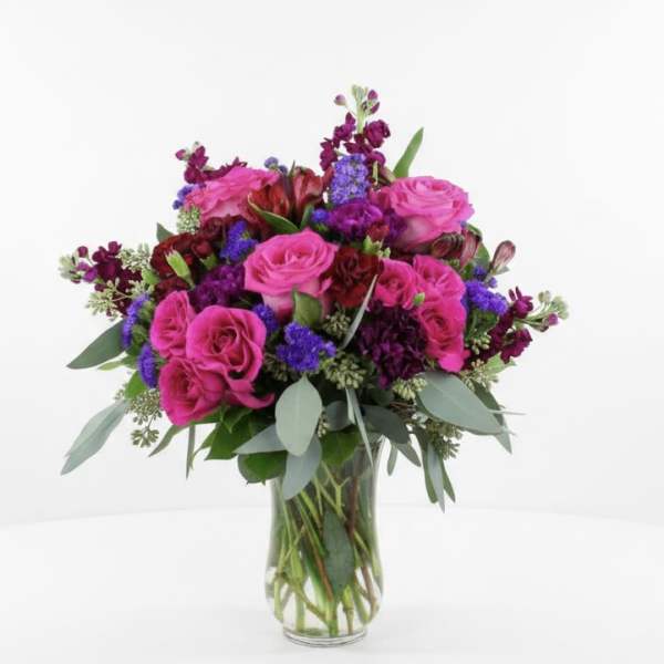 Pink roses and purple flowers arranged in a clear glass vase
