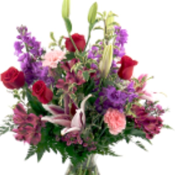 Tall mixed bouquet of red roses, pink lilies, and purple flowers in a clear glass vase