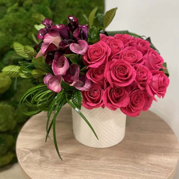 Hot pink roses and purple calla lilies in a white cylinder vase on a wooden table