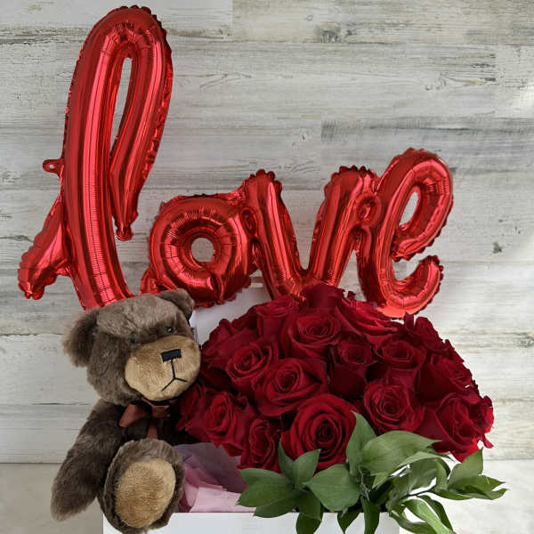 Red roses in a white box with a teddy bear and red "Love" balloon