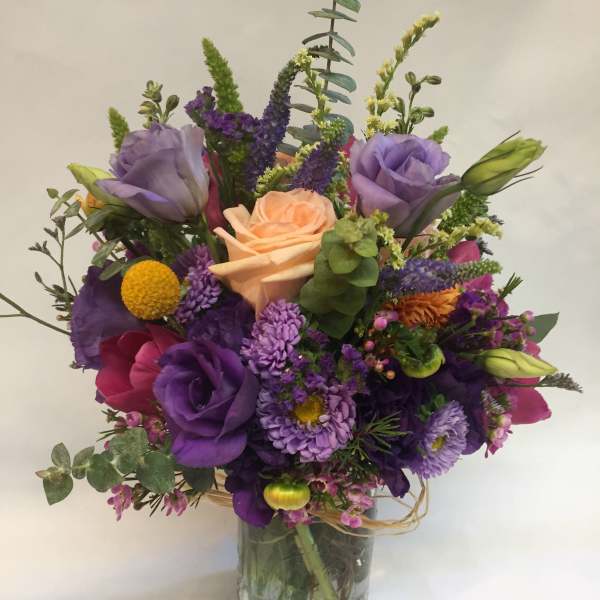 Mixed bouquet of purple, peach, and pink flowers in a glass vase