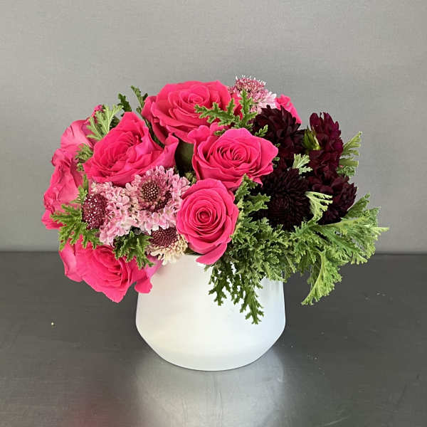 Pink roses and dark blooms arranged in a white vase