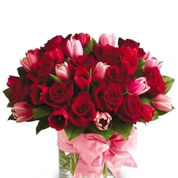Red roses and pink tulips in a glass vase with a pink ribbon