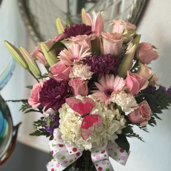 Tall pink and white mixed flower arrangement in a glass vase with ribbon and butterfly decoration