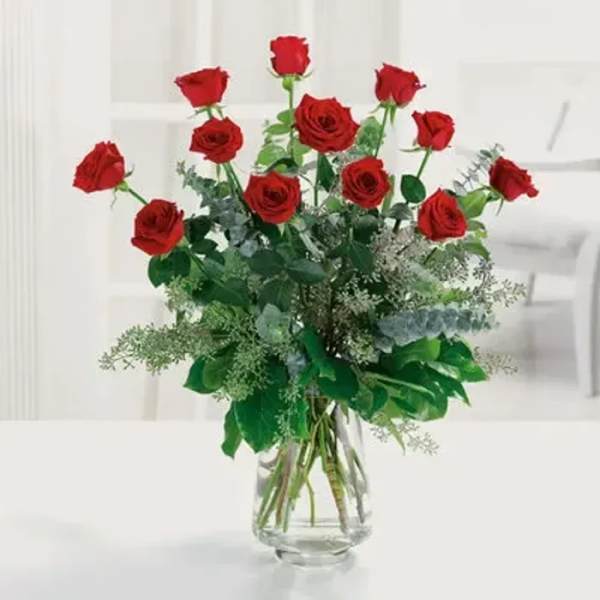 Tall arrangement of long-stem red roses with lush greenery in a clear glass vase