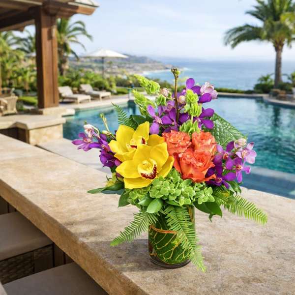 Tropical bouquet with yellow orchids, purple flowers, and orange blooms in a glass vase