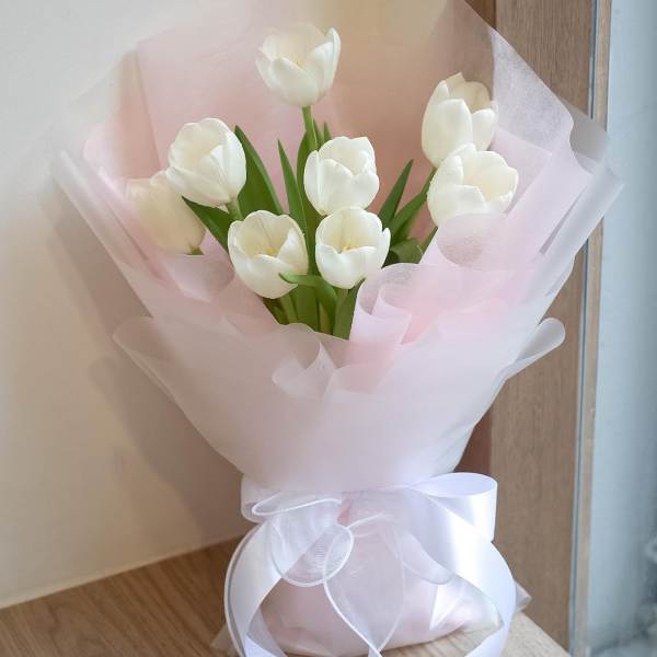 White tulip bouquet wrapped in pale pink paper with a white ribbon