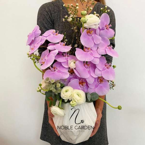 Woman holding a white vase filled with lavender orchids and white blooms