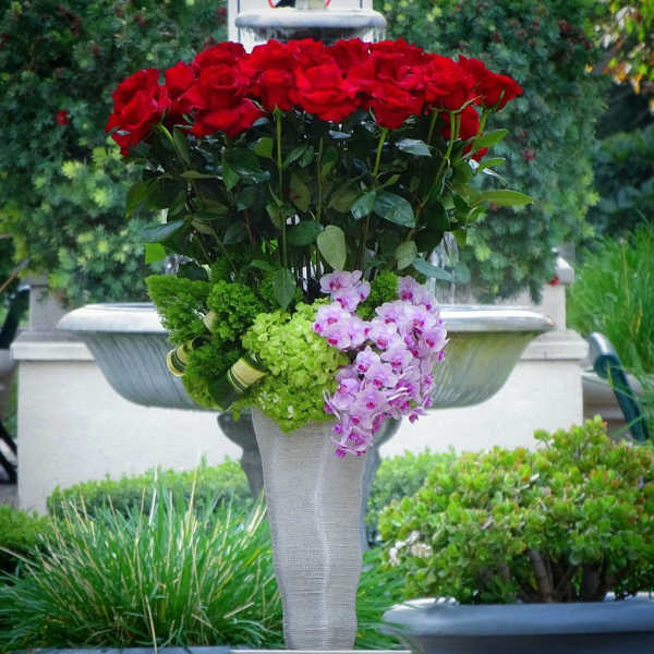 Tall arrangement of red roses with pink orchids and green hydrangeas in a pedestal vase