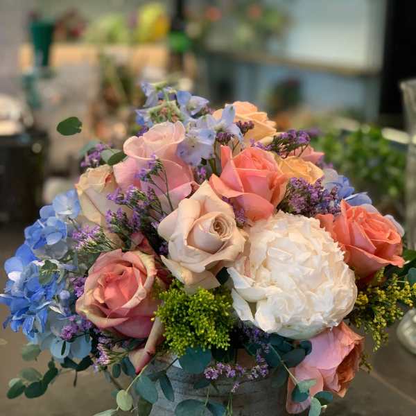 Mixed bouquet of pastel roses and blue flowers in a gray container