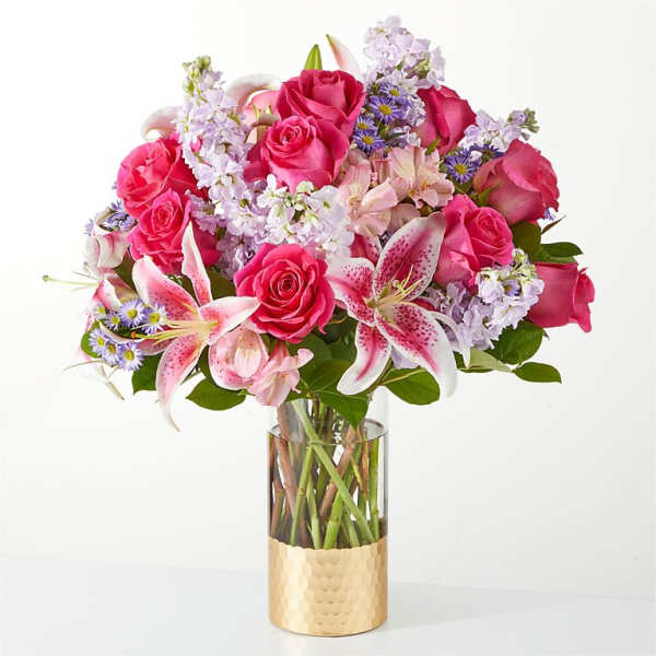 Pink roses and lilies arranged in a glass vase with a gold base