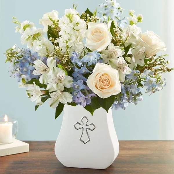 White and pale blue flower arrangement in a white vase with a cross emblem