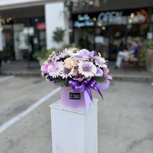Lavender and white bouquet in a pink hatbox with a purple ribbon