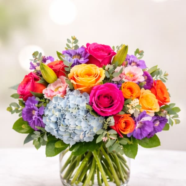 Colorful bouquet of roses, hydrangea, and lilies in a glass vase