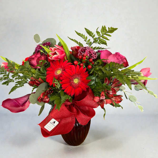 Red and pink mixed bouquet in a dark vase with a red ribbon