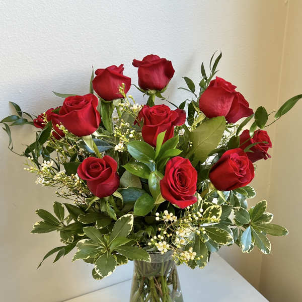 Red roses arranged in a clear glass vase with mixed greenery