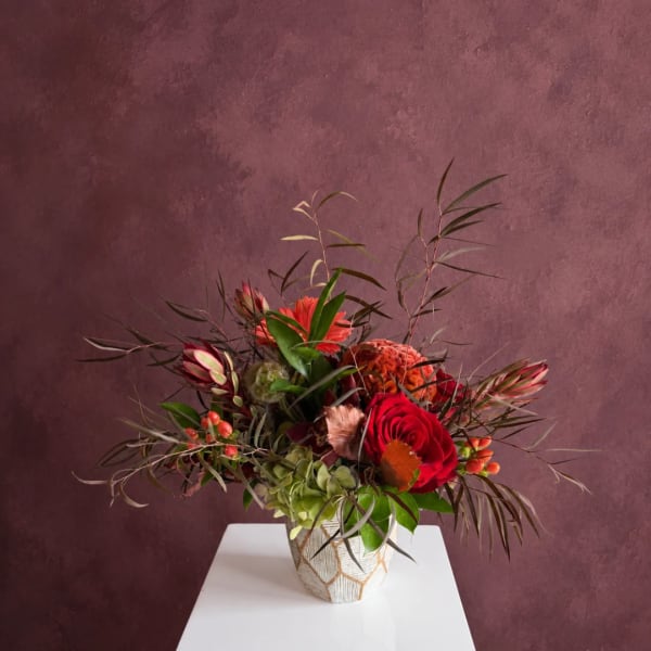 Mixed floral arrangement with red roses in a patterned vase