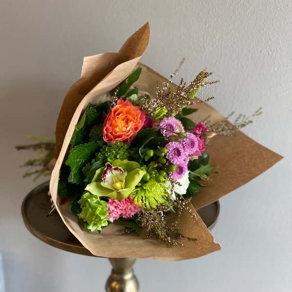 Mixed bouquet with orange, pink, and green flowers wrapped in brown paper