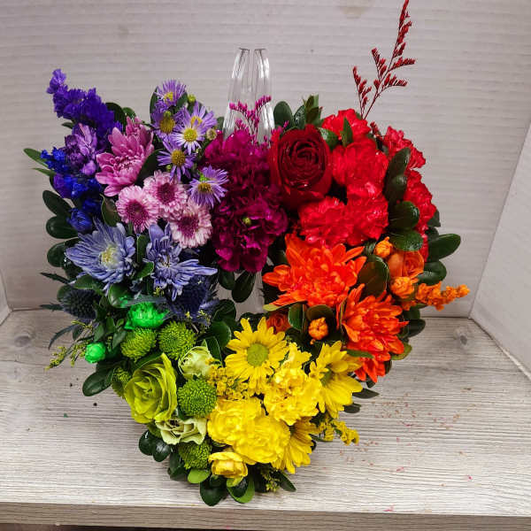 Heart-shaped bouquet of multicolored flowers with a clear vase in the center