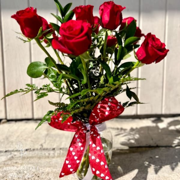 Red roses in a clear glass vase with a red heart-pattern ribbon