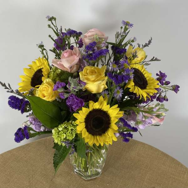 Mixed bouquet of sunflowers, yellow and pink roses in a clear glass vase