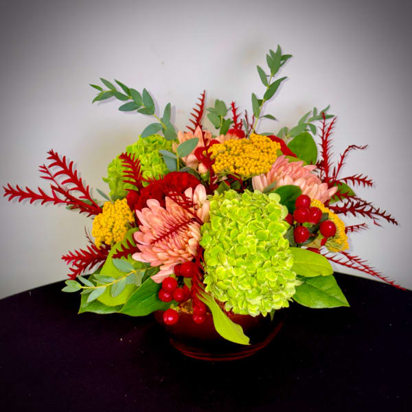 Colorful floral arrangement in a low red vase with pink, green, and yellow blooms