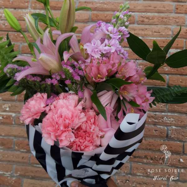Pink bouquet with lilies, carnations, and small purple flowers in striped wrap