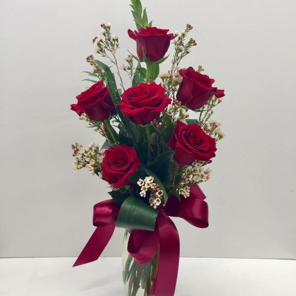 Red roses arranged in a clear glass vase with a burgundy ribbon