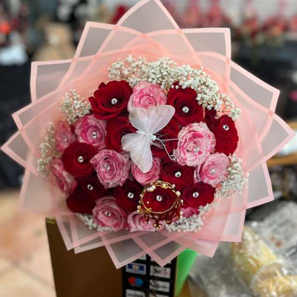 Bouquet of red and pink roses wrapped in pale pink paper with a butterfly topper