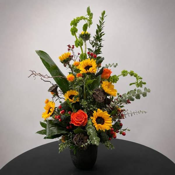 Tall mixed floral arrangement with sunflowers and orange roses in a black vase