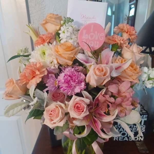 Bouquet of peach and pink flowers in a glass vase with a pink "I Love You" pick
