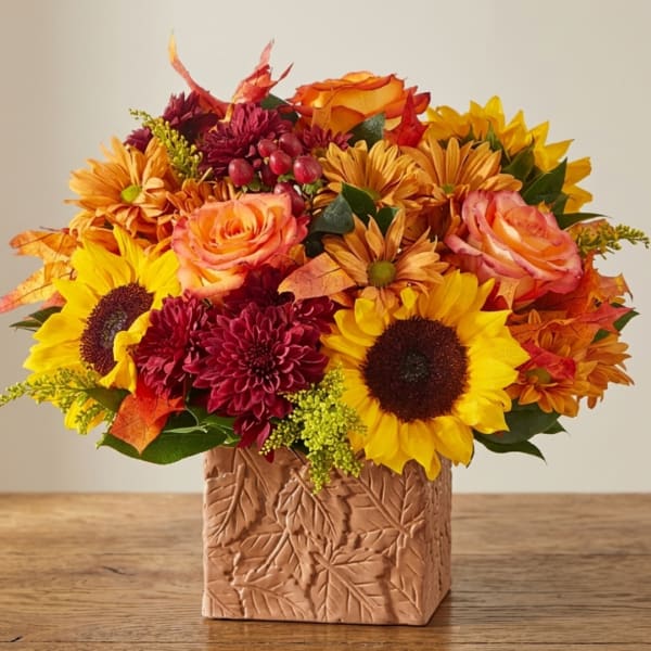 Autumn bouquet with sunflowers, roses, and mums in a leaf-patterned vase