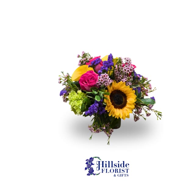 Colorful mixed bouquet with sunflower, pink rose, and purple accents in a glass vase