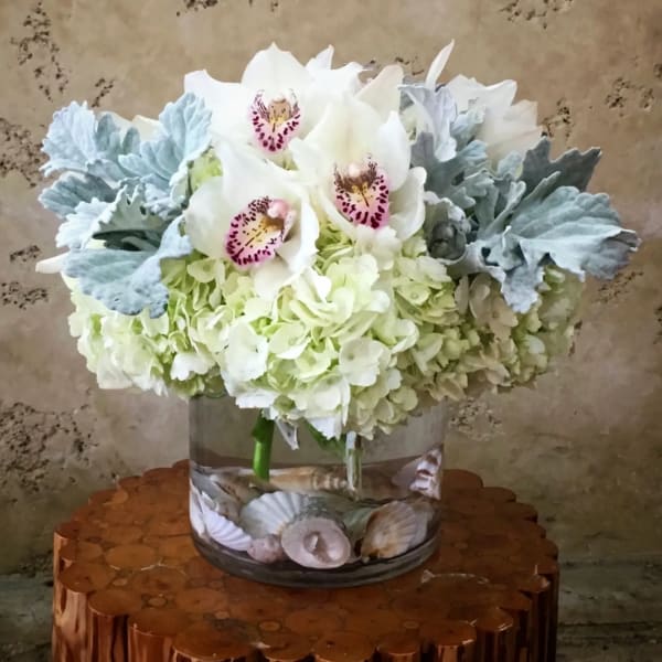White orchids and pale hydrangeas in a glass vase with seashells
