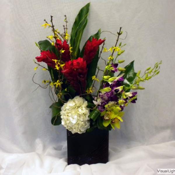 Tropical floral arrangement with red and purple blooms in a black vase